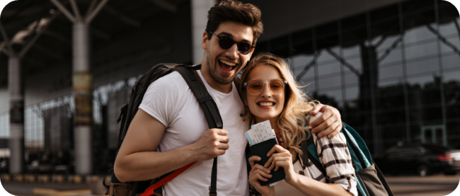 Imagem jovem morena-sorri-amplamente-e-abraca-sua-namorada-atraente-casal-de-viajantes-segura-mochilas-e-passaportes-no-fundo-do-aeroporto